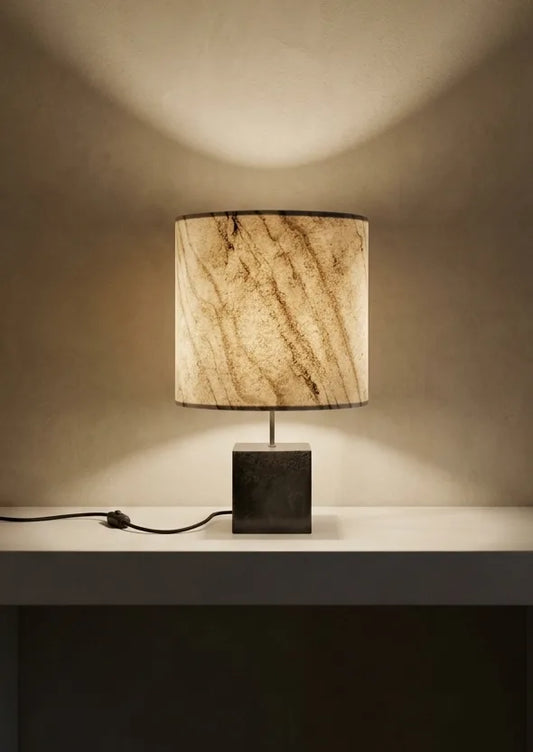 Lampe en acier et marbre statuaire sur une console en pierre contre unmur clair en béton ciré. modèle Cassini Nova de l'ateier Maus