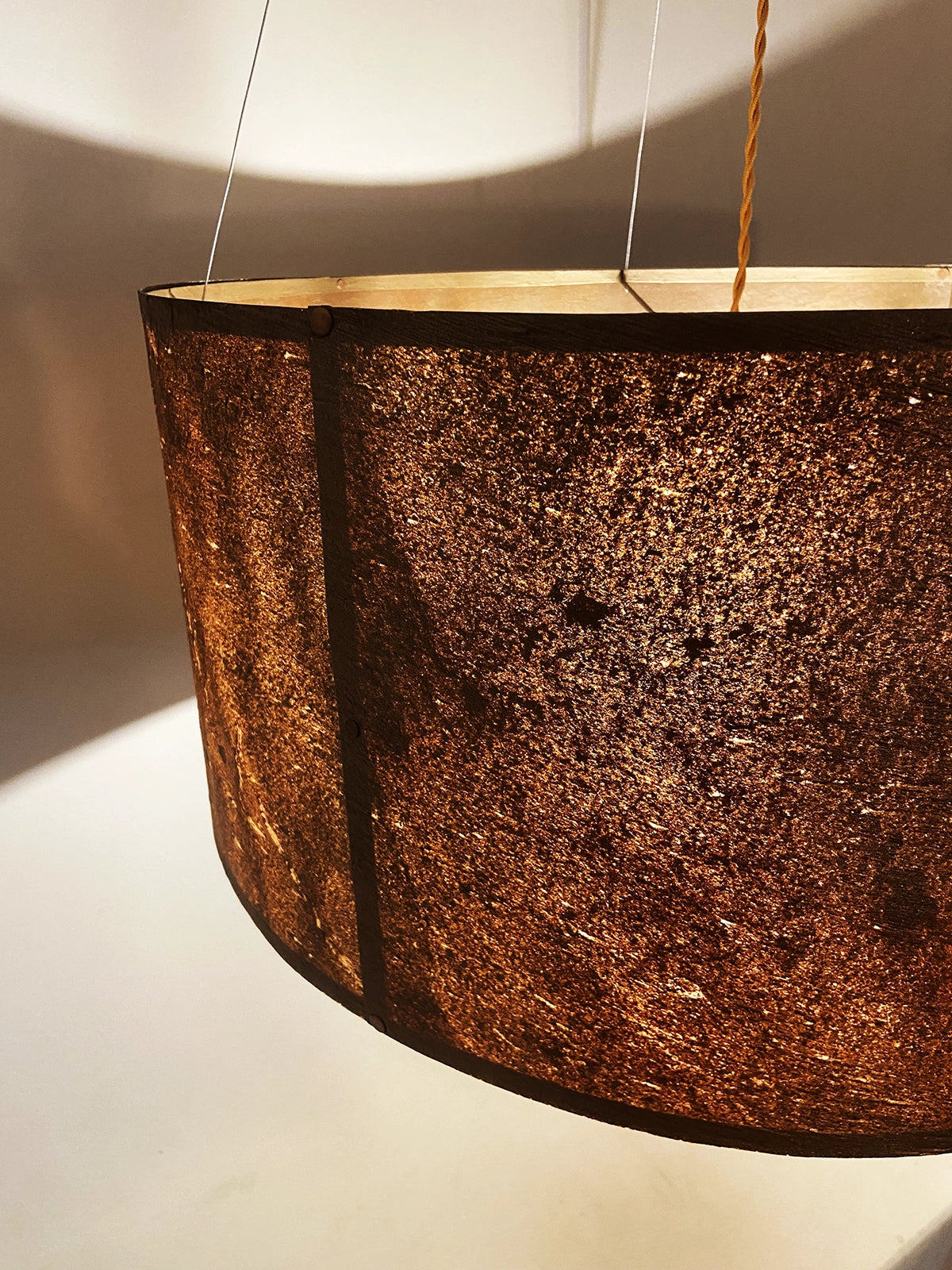 Détail de la suspension en feuille de mica cuivré Thessalie par l'atelier Maus allumée. Rosace et carcasse en acier cuivré, suspendue par 4 cables inox de longueur réglable. Pièce artisanale unique de fabrication française.