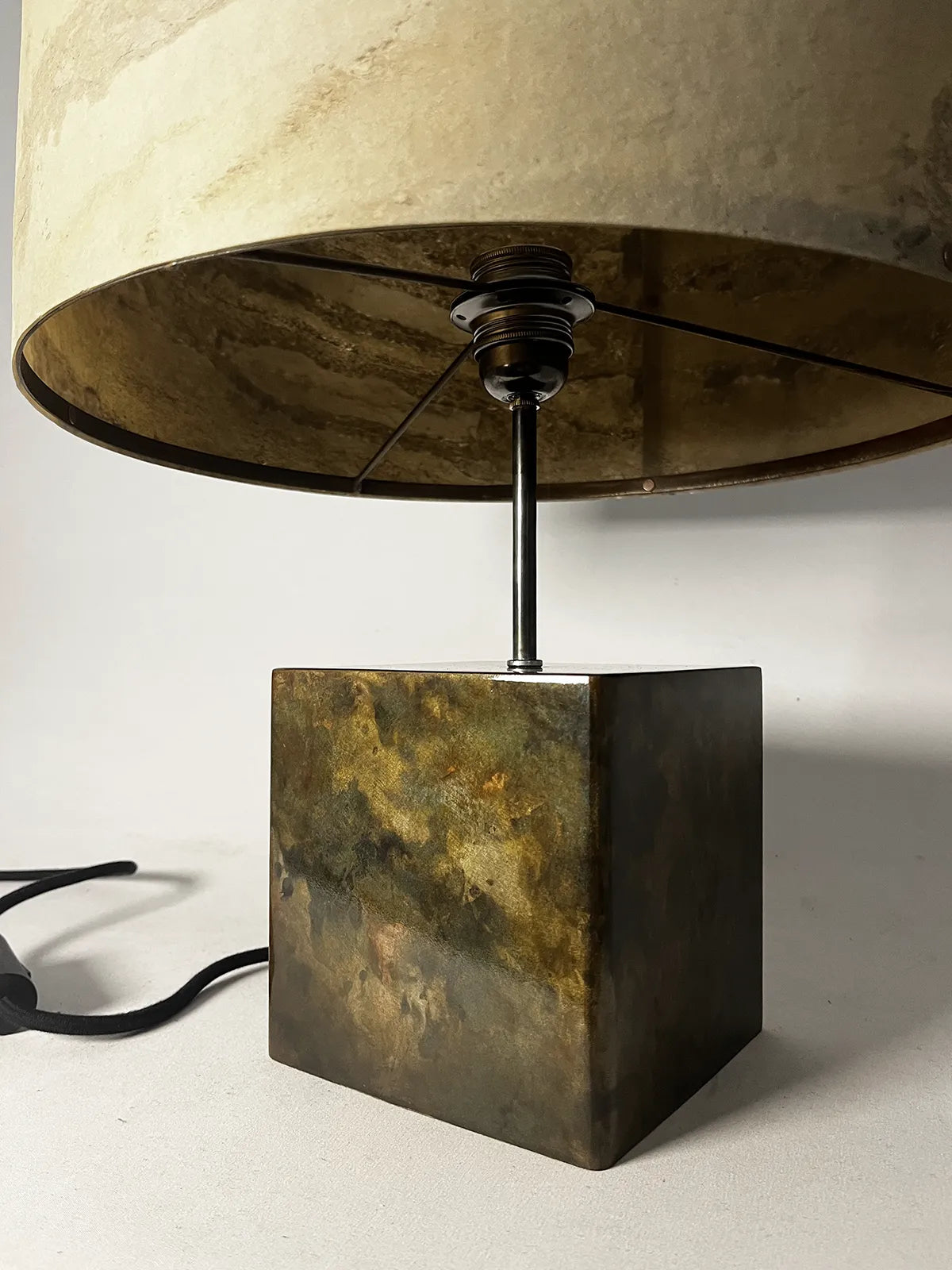 Vue de détail du piètement en acier patiné irisé de la lampe Cassini par l'atelier Maus, surplombée de son abat-jour en feuille d'ardoise beige, ocre et brune