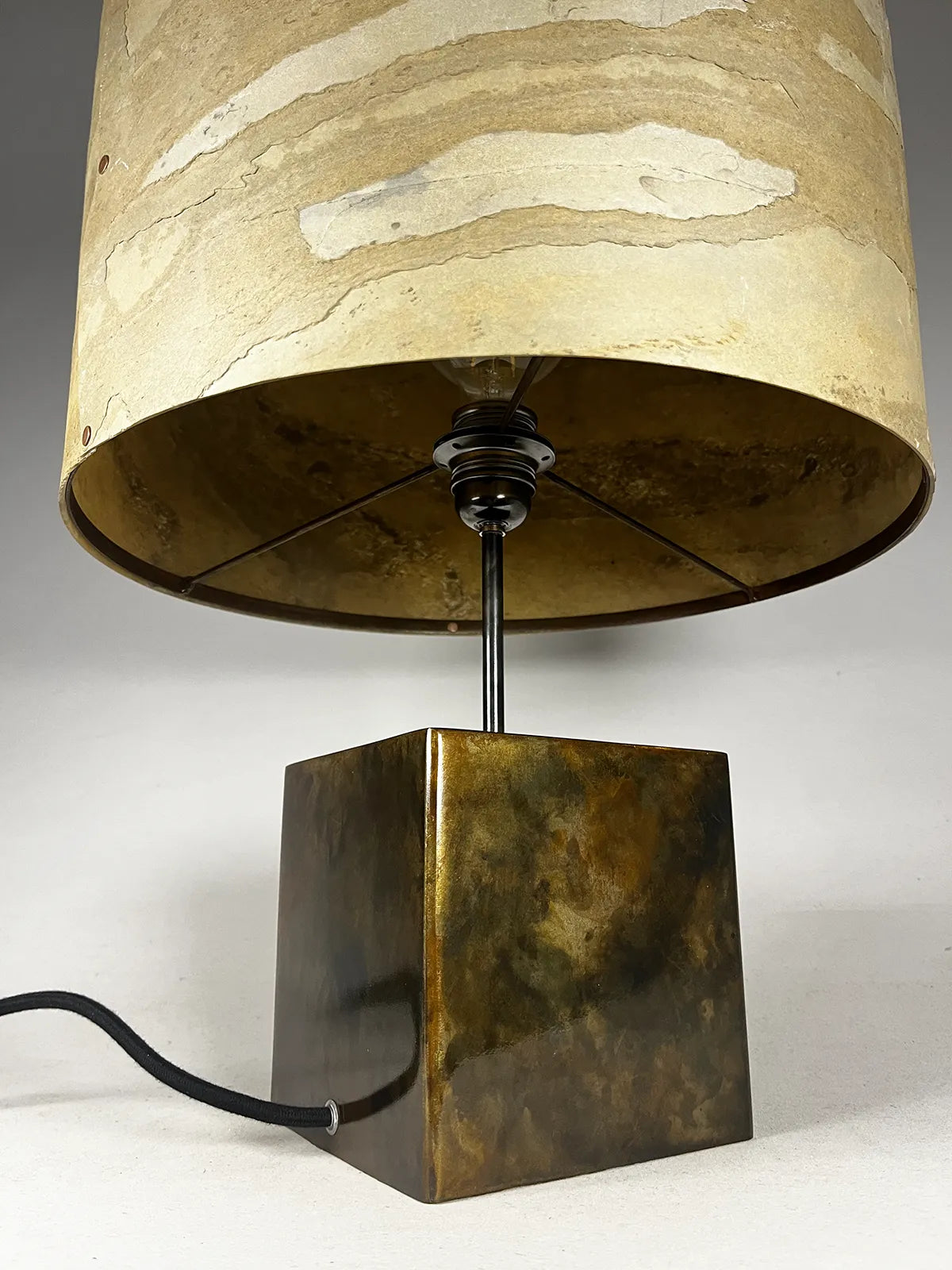 Vue en contre plongée de la Lampe Cassini Aura de l'atelier Maus éteinte. Piètement cubique aux couleurs irisées et abat-jour texturé en feuille d'ardoise naturelle nuancée de beiges, ocres et brun
