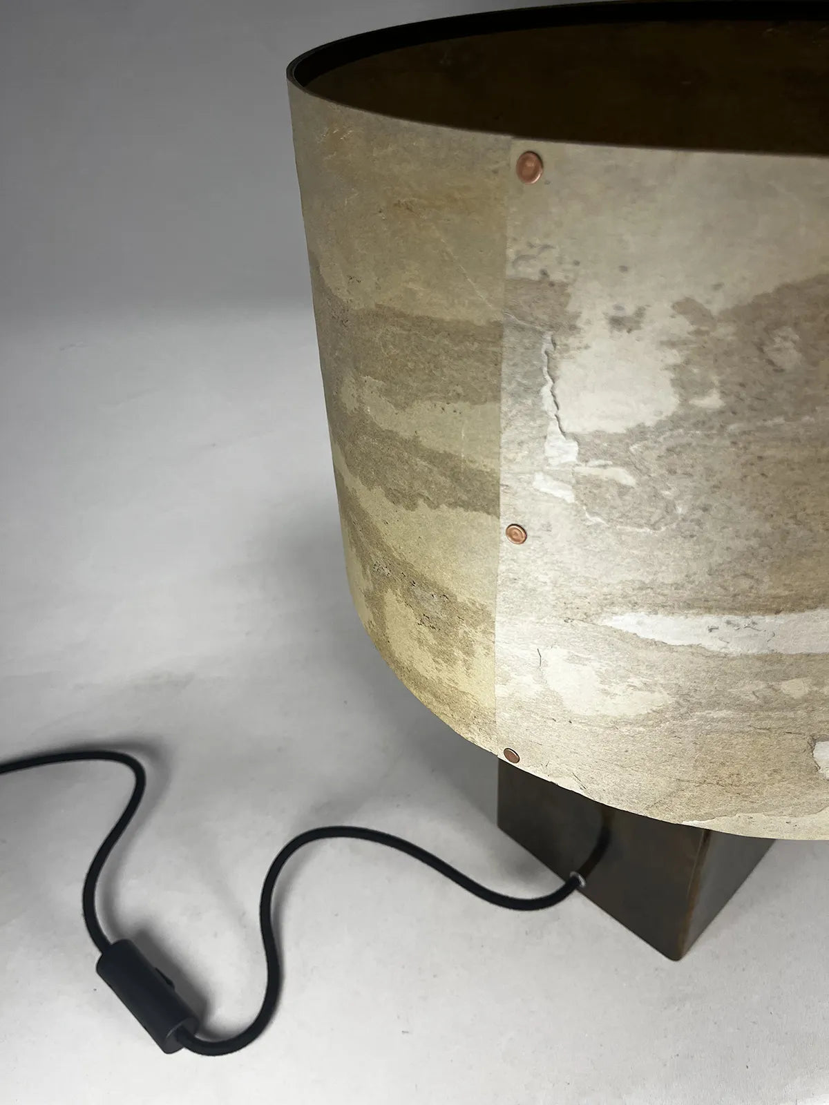 detail de l'abat-jour de la Lampe à poser Cassini Aura éteinte. Abat-jour en feuille d'ardoise nuancée de beiges, ocres et brun et fixation par rivets cuivre