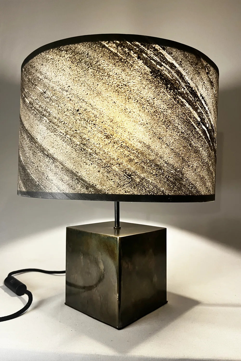 Vue de profil lampe Cassini Aura – zébrures minérales de l'ardoise naturelle et patine noire brune irisée du pied en acier