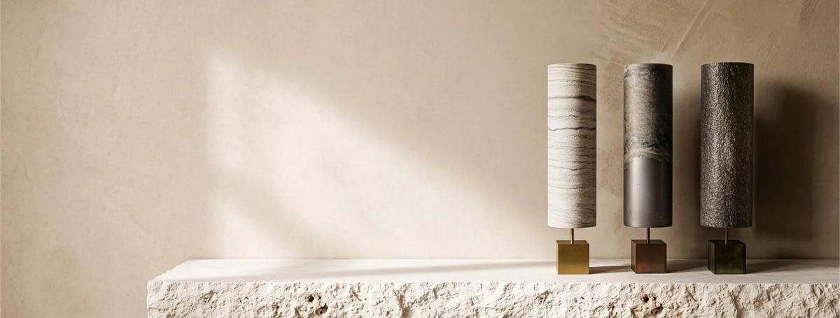 Bannière héro du site de l'atelier Maus représentant 3 lampes modèle Halley à droite sur un plan en pierre blanche brute contre un mur en béton ciré couleur blanc cassé
