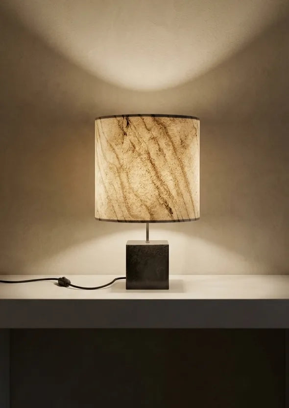 Lampe en acier et marbre statuaire sur une console en pierre contre unmur clair en béton ciré. modèle Cassini Nova de l'ateier Maus