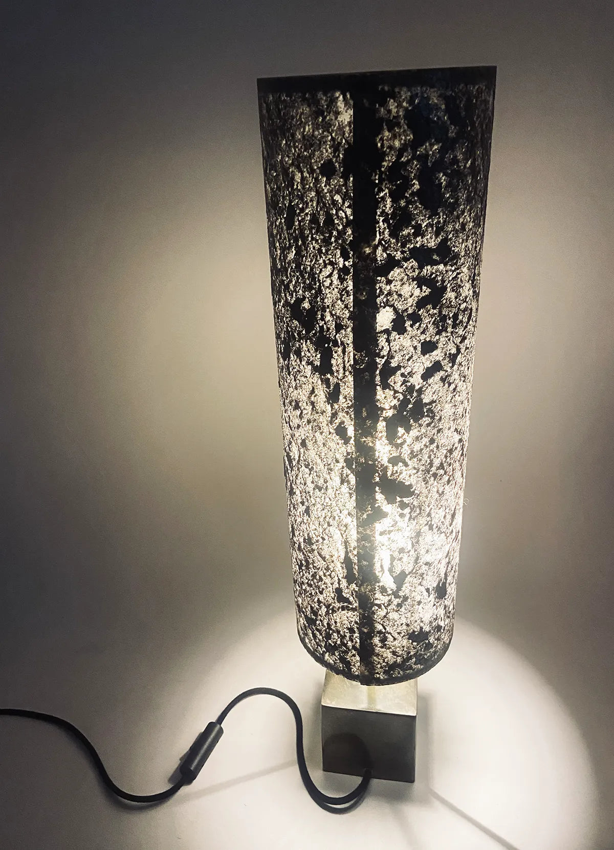 Vue arrière de la Lampe artisanale unique en acier patiné  et feuille de mica argenté allumée. création originale de l'atelier Maus. Fabriqué en France