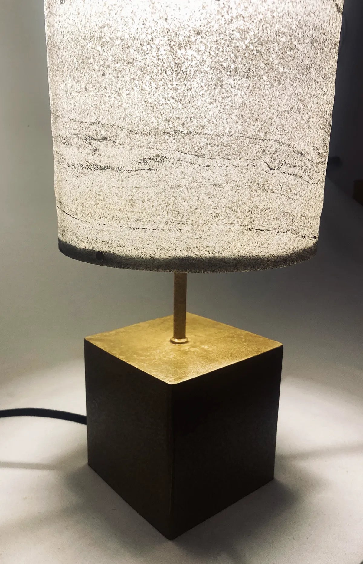 Vue de détail de la lampe en acier laitonné et abat-jour en marbre statuario allumée. Pièce unique de l'atelier Maus. Fabriqué en France