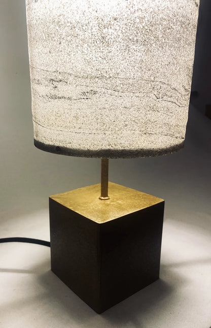 Vue de détail de la lampe en acier laitonné et abat-jour en marbre statuario allumée. Pièce unique de l'atelier Maus. Fabriqué en France